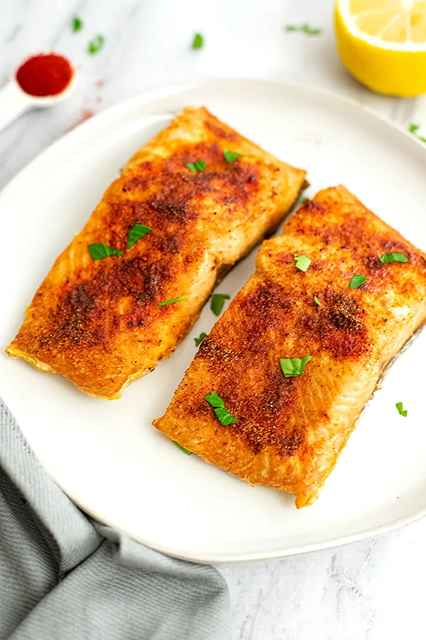 Two pieces of air fryer salmon on a white plate.