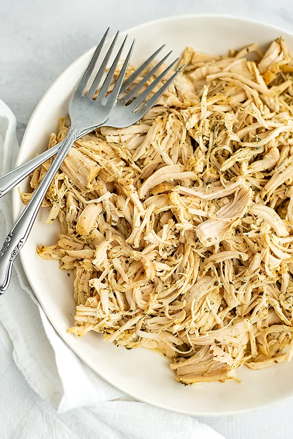 White plate filled with crockpot ranch chicken after shredding.