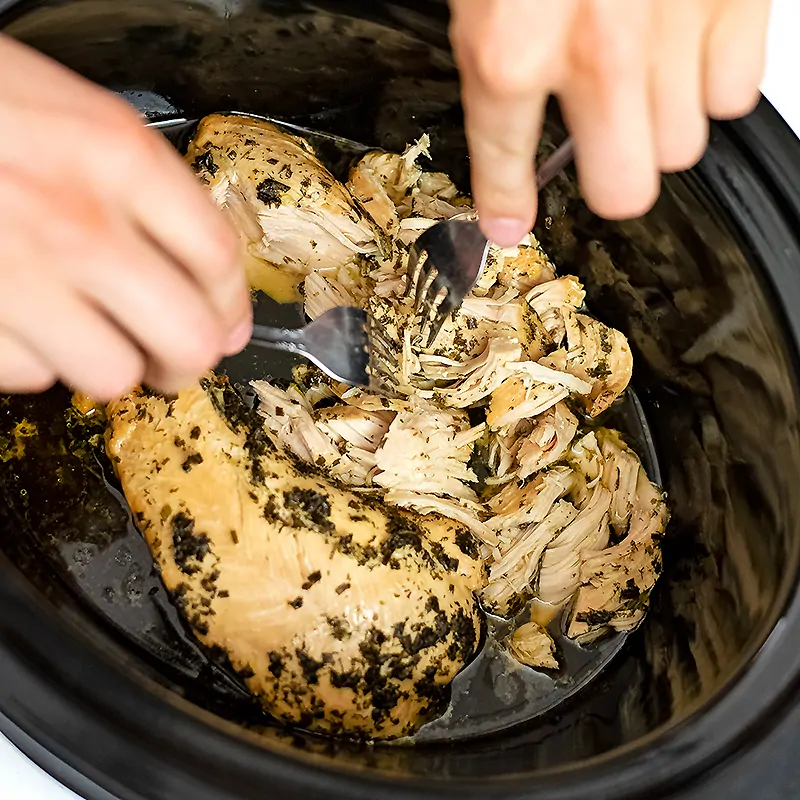 Two hands shredding crockpot ranch chicken.