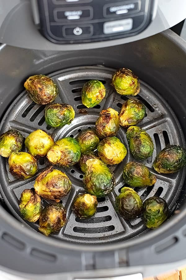 Frozen brussel sprouts in an air fryer basket after cooking.
