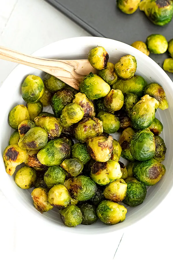 Large bowl filled with roasted brussel sprouts and a wooden spoon.