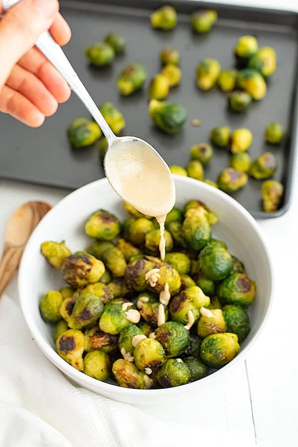 Spoon drizzling tahini over roasted brussel sprouts.