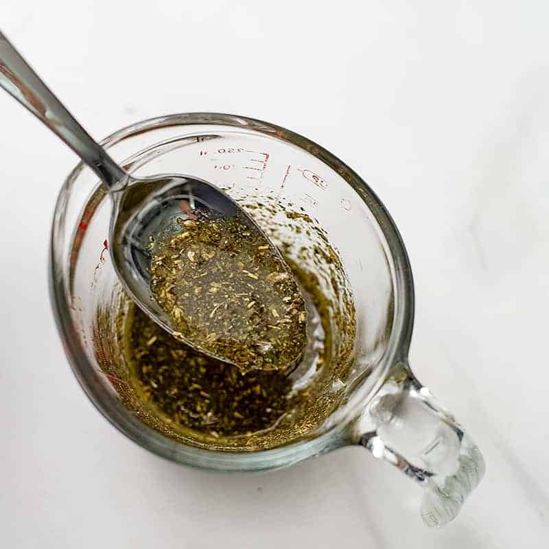 Glass measuring cup filled with greek marinade with a spoon in the cup.