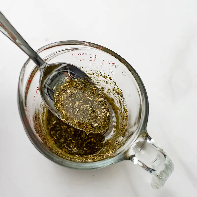 Glass measuring cup filled with greek marinade with a spoon in the cup. 