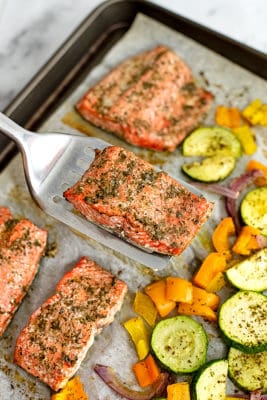 Spatula holding a piece of greek salmon over the sheet pan.