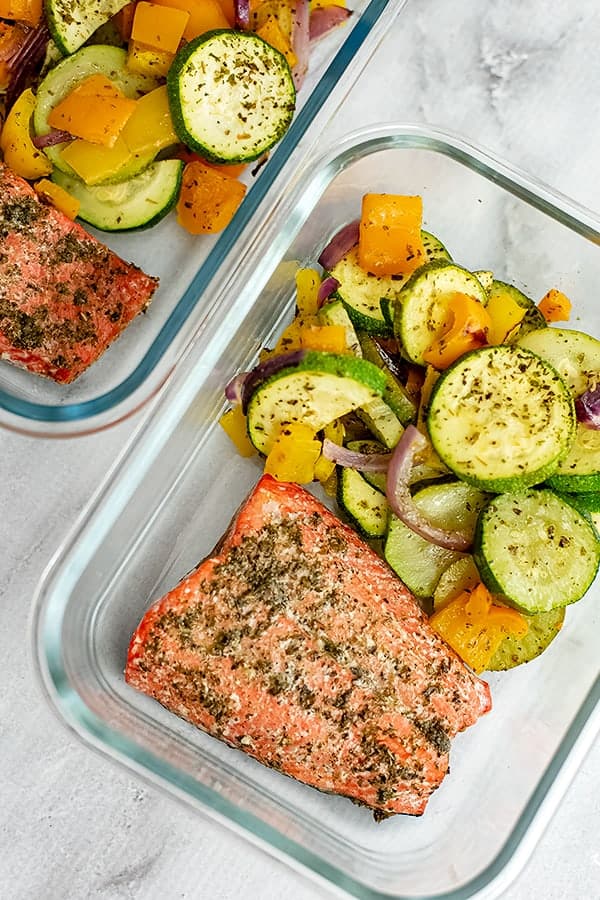 Glass storage container filled with Greek salmon and vegetables. 