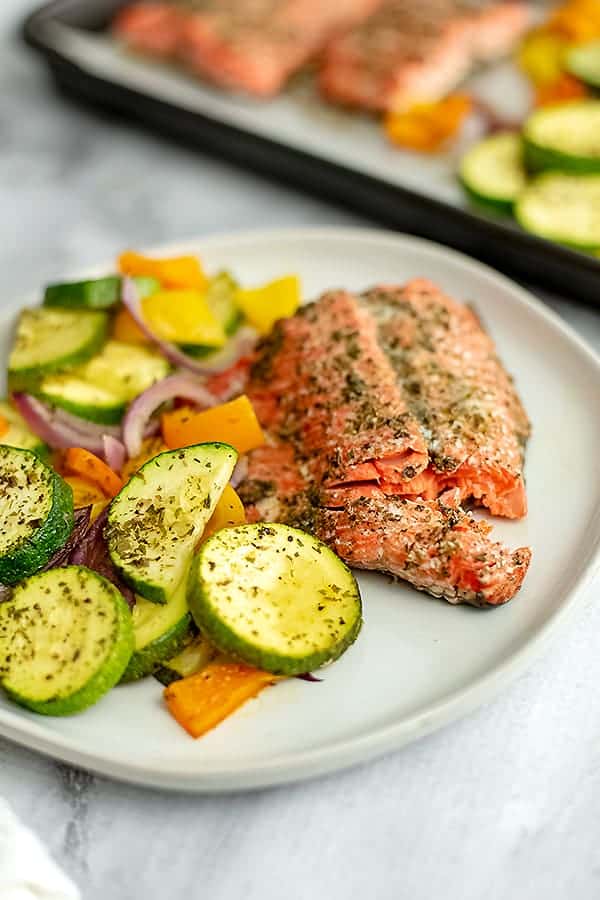 Flaked salmon on a plate next to greek vegetables. 
