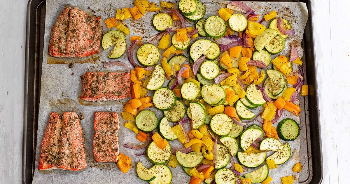 Baking sheet filled with cooked greek salmon and vegetables. 