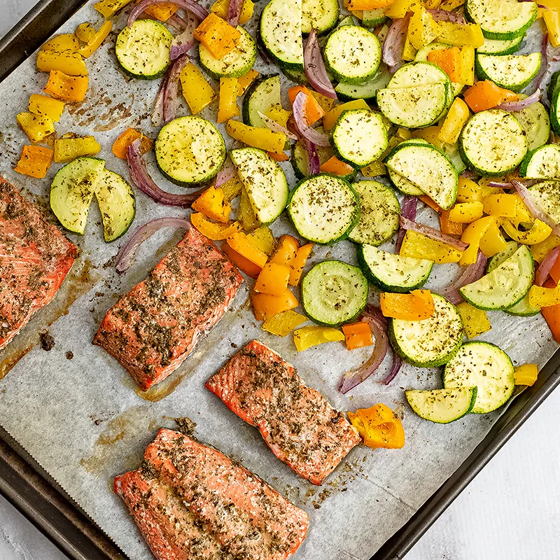 Greek salmon and veggies on a baking sheet after baking.