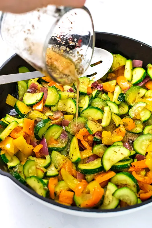 Greek marinade being poured over skillet of veggies.
