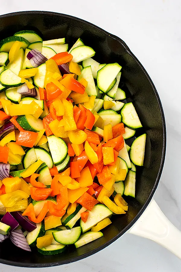 Sliced vegetables in a large cast iron skillet before cooking.