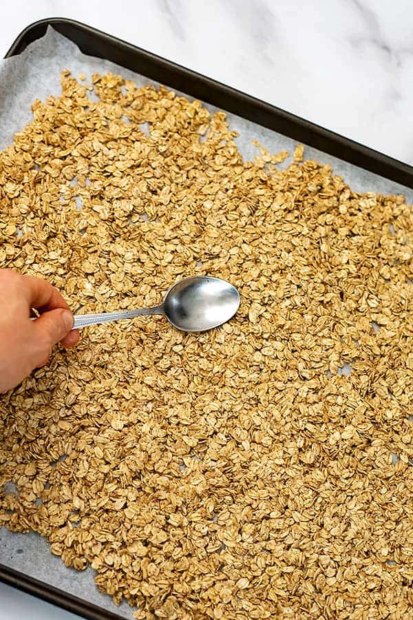 Baking sheet with raw granola being spread out with spoon.