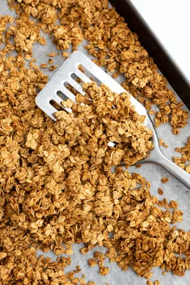 Silver spatula on baking sheet full of granola.