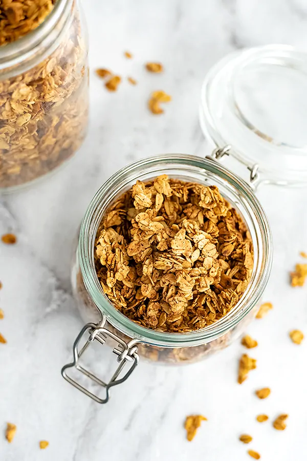 Glass container filled with vegan granola with granola around the jar.