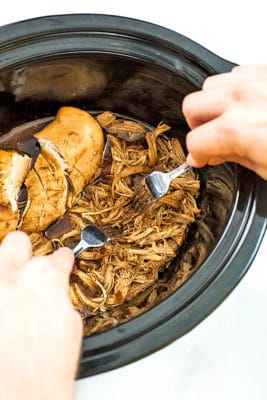 Two forks shredding the balsamic chicken in the slow cooker.