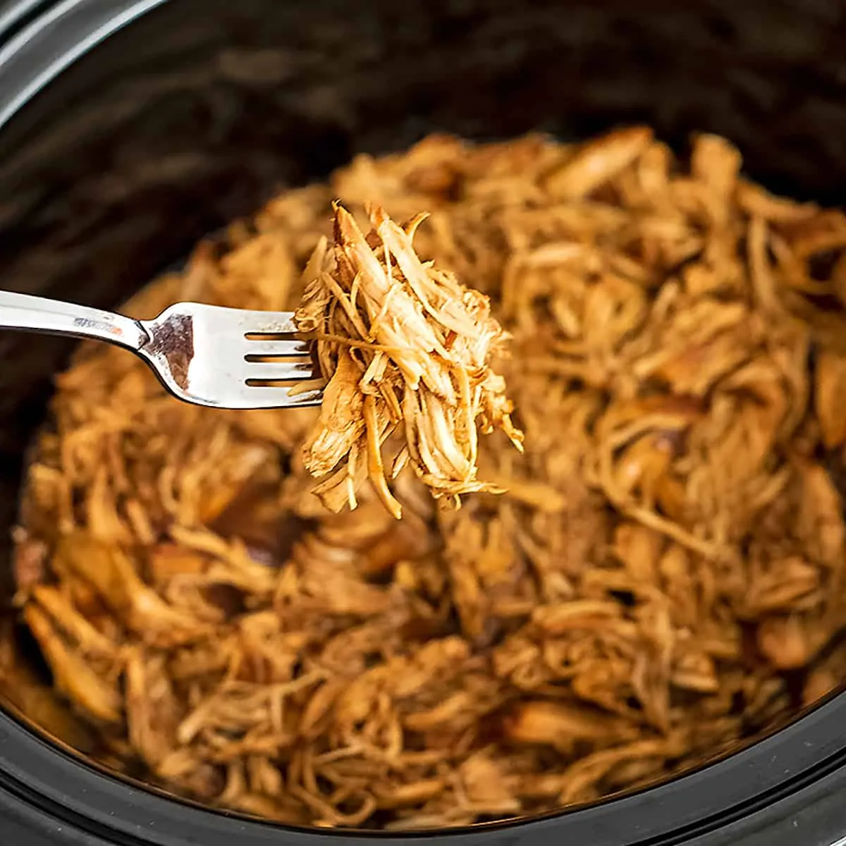 Fork holding shredded balsamic chicken over a crock pot.