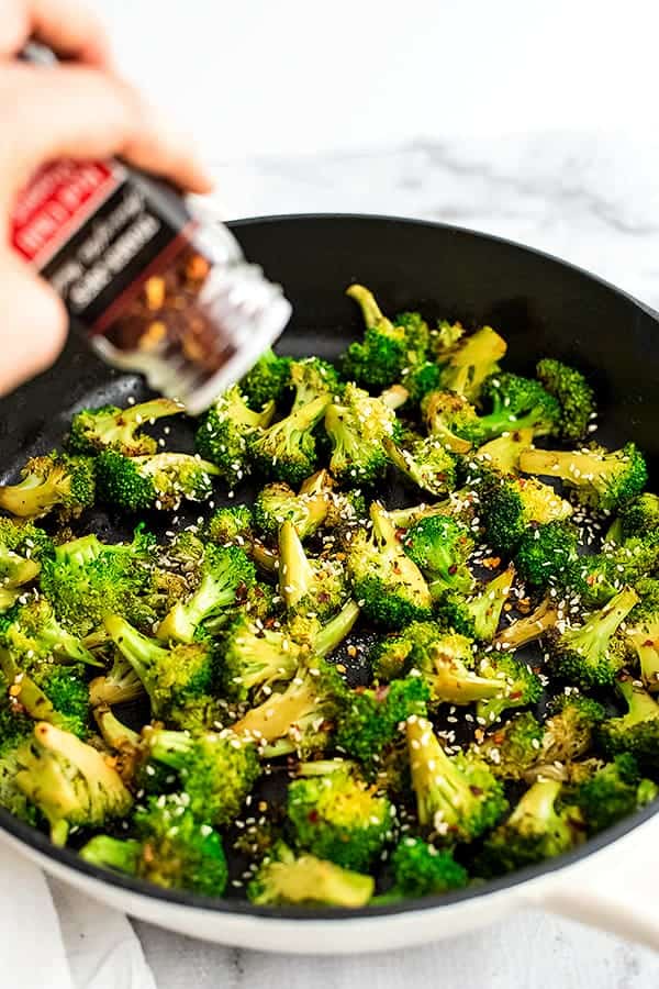 Red pepper flakes being sprinkled on a skillet of broccoli.