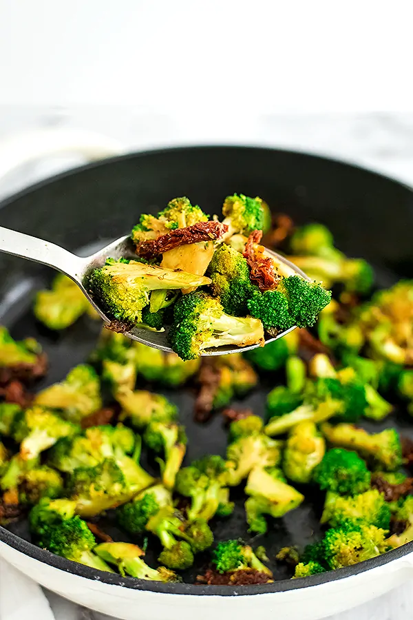 Silver serving spoon filled with sun dried tomato broccoli.
