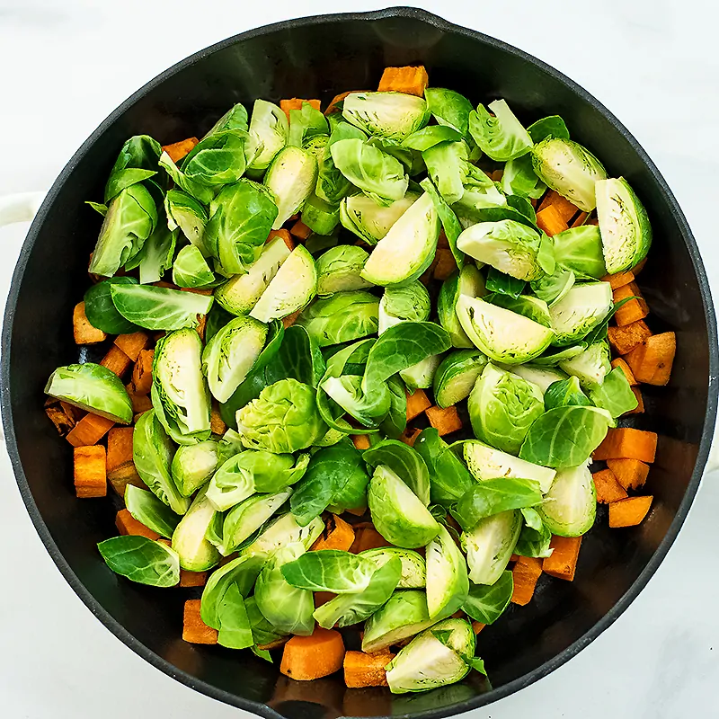 Quartered brussels sprouts over sweet potatoes in skillet.