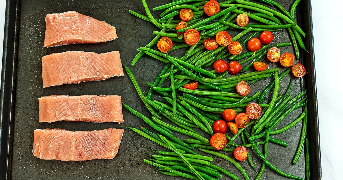 Sheet pan with salmon filets, green beans and tomatoes.