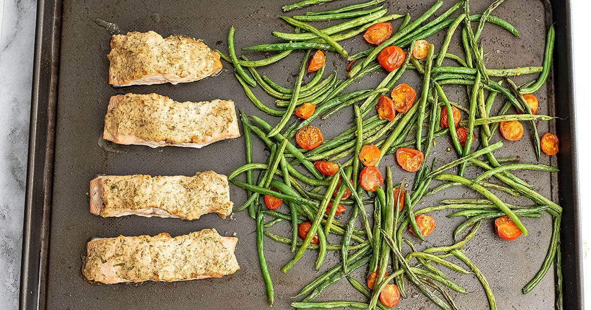Sheet pan with cooked tahini herb crusted salmon, green beans and tomatoes. 