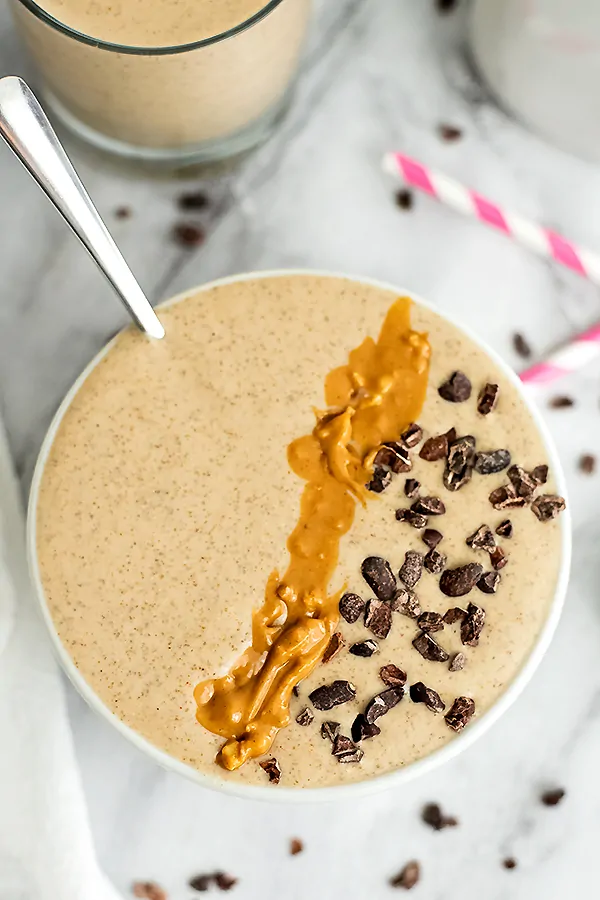 Peanut butter smoothie in white bowl with toppings and spoon in bowl.