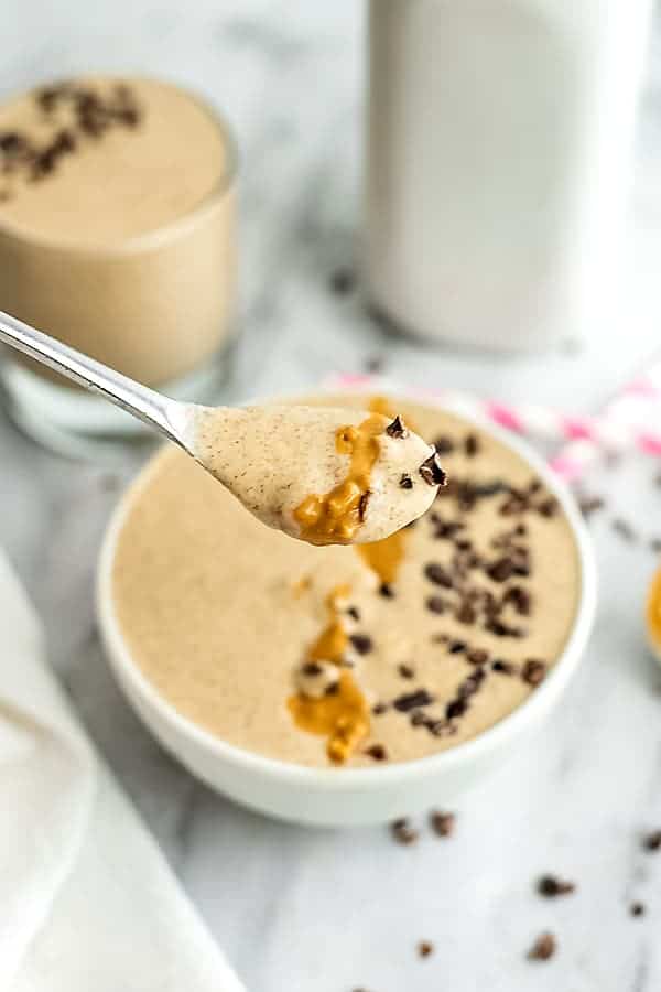 Spoon holding peanut butter smoothie over a bowl.