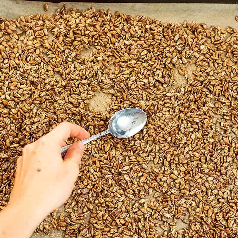 Spiced sunflower seeds being spread on a baking sheet.