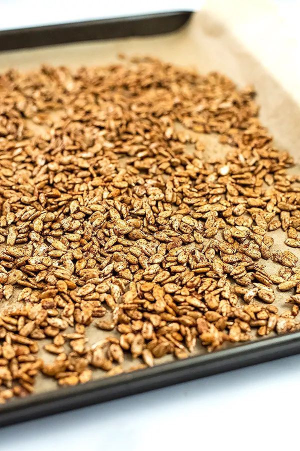 Pumpkin spice sunflower seeds spread out on a baking sheet.