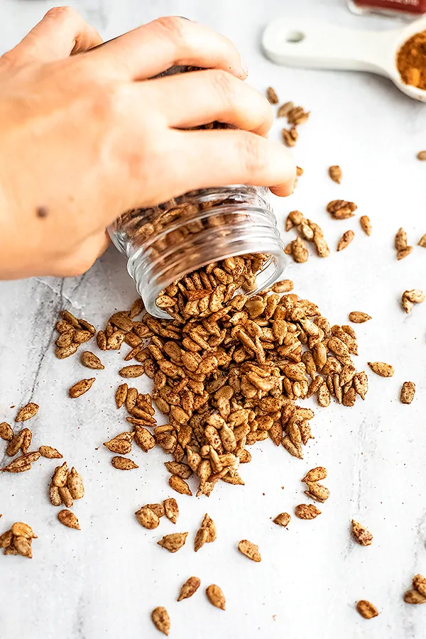 Hand pouring out a glass jar of spiced sunflower seeds.