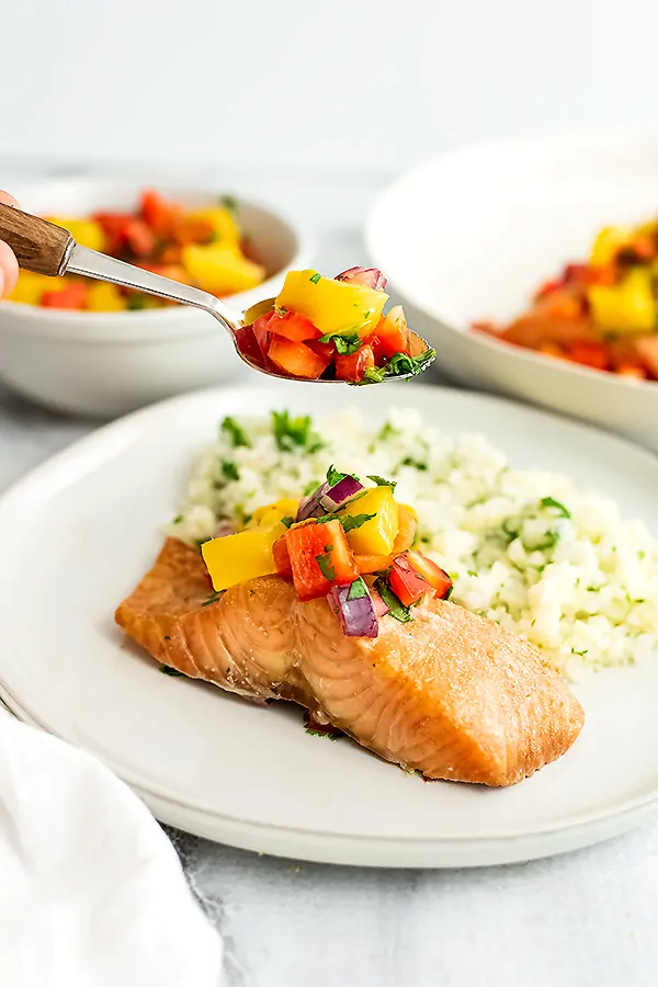 Salmon filet on a white plate with mango salsa spooning on top.