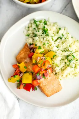 Mango salsa salmon with cauliflower rice on a white plate.