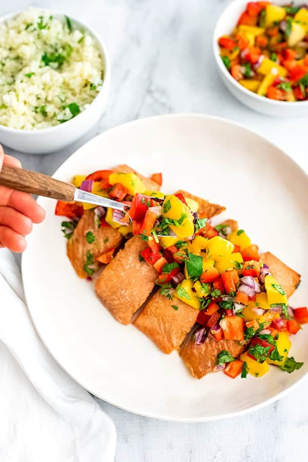 4 pieces of salmon on a serving dish with mango salsa being spooned on.