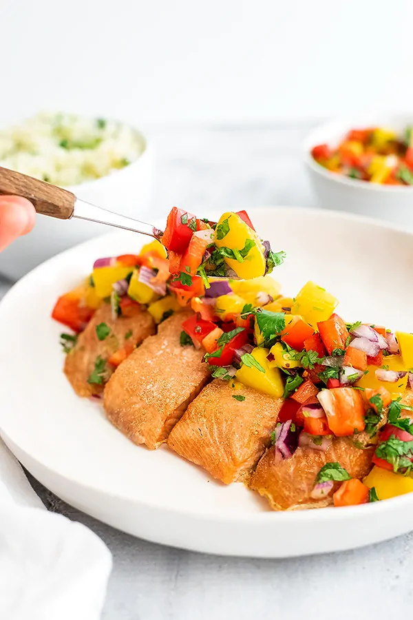Mango salsa being spooned on top of salmon fillets. 