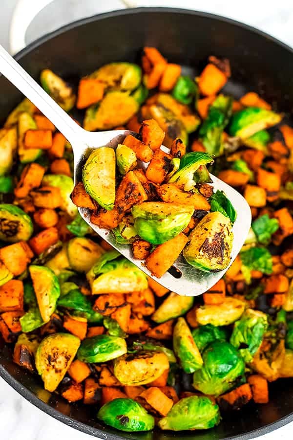 Sweet potato breakfast hash being held by a silver spatula over skillet.
