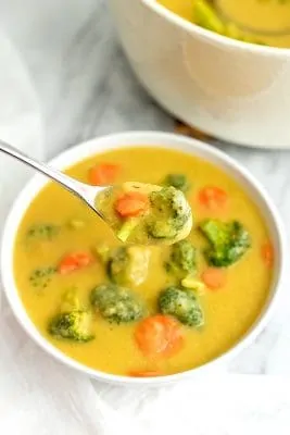 Spoon full of broccoli cheese soup over a bowl.