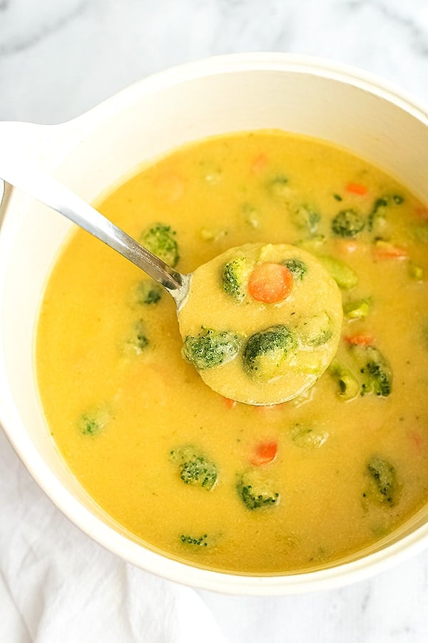Large ladle full of broccoli cheese soup over a pot of soup.