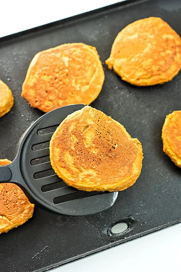 Spatula holding a pumpkin pancake after cooking over a griddle.