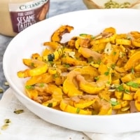 Bowl filled with roasted delicata squash with tahini in background.