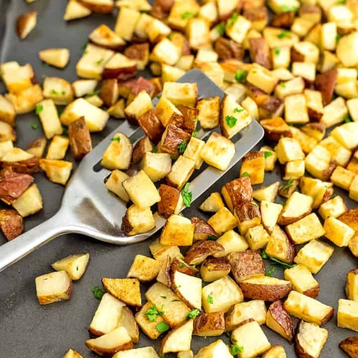 Roasted potatoes on a baking sheet with a silver spatula.
