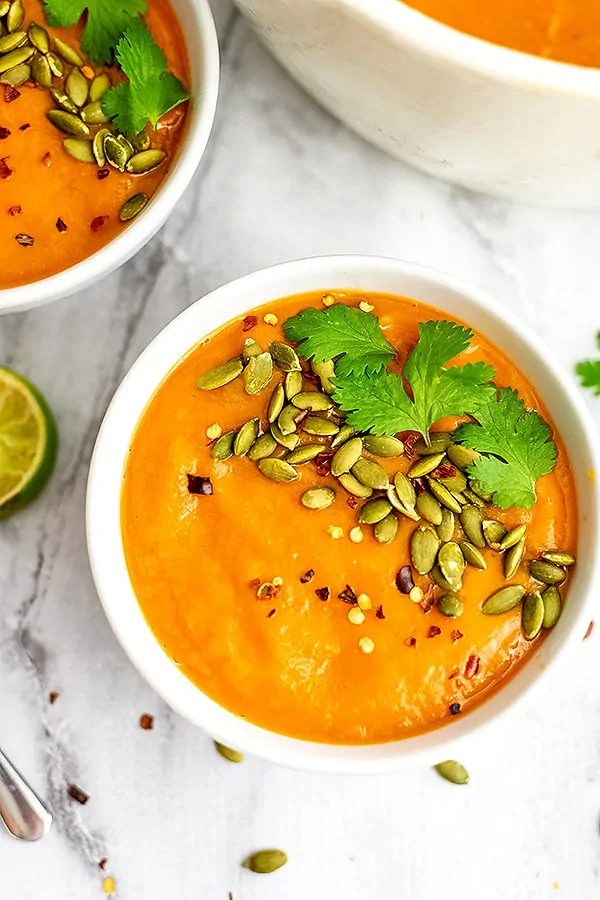 Sweet potato red pepper soup in a white bowl with toppings.