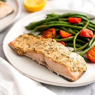 Plate filled with tahini herb crusted salmon, green beans and tomatoes.