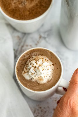 Hand holding handle of mug of protein hot chocolate.
