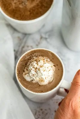 Hand holding handle of mug of protein hot chocolate.