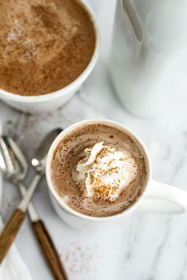 Mug full of protein hot chocolate with spoons to the left.