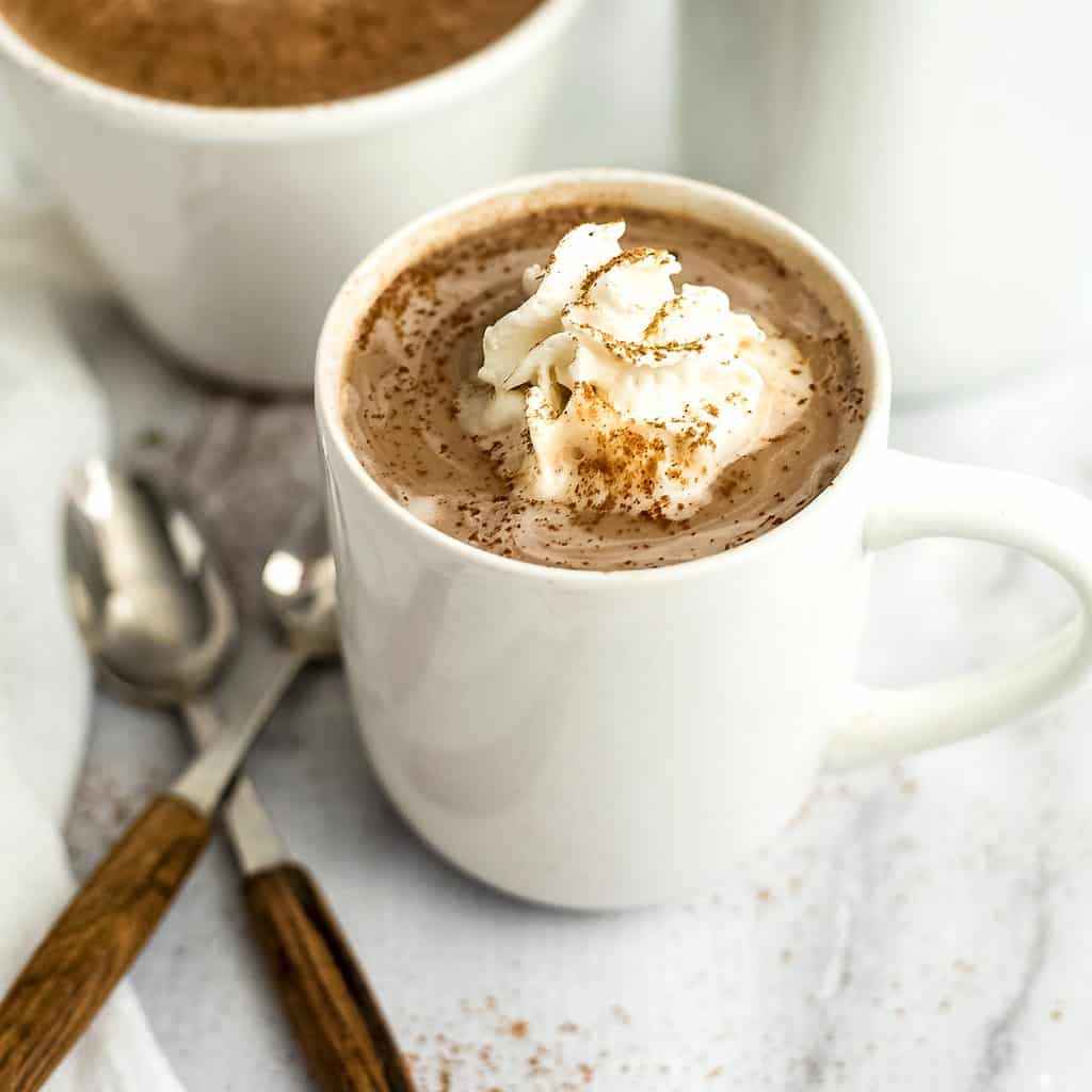 Protein hot chocolate topped with whipped cream in a white mug.