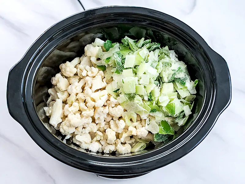 Slow Cooker filled with frozen cauliflower and frozen leeks.