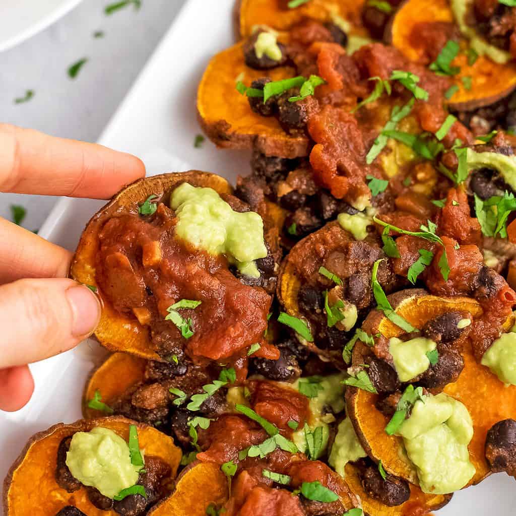 Hand holding a single sweet potato black bean nacho.