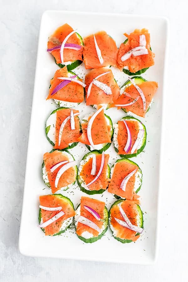 White rectangle plate filled with smoked salmon cucumber bites.