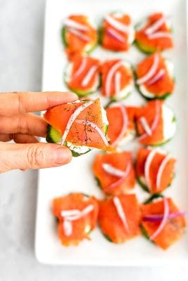 Hand holding single cucumber smoked salmon bite.